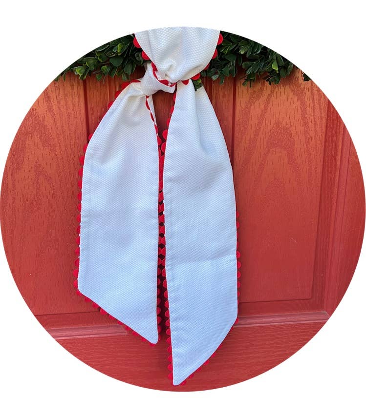 White cotton pique sash with red scalloped trim tied on a boxwood wreath over a red front door