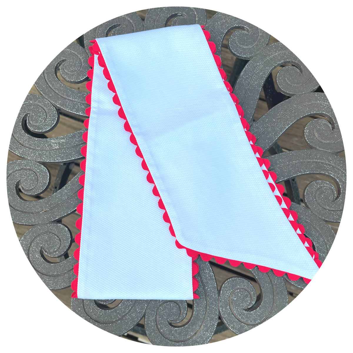 Folded white cotton pique fabric with red scalloped trim, styled on an ornate metal outdoor table
