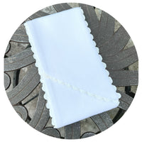 Folded white cotton pique fabric with white scalloped trim, styled on an ornate metal outdoor table