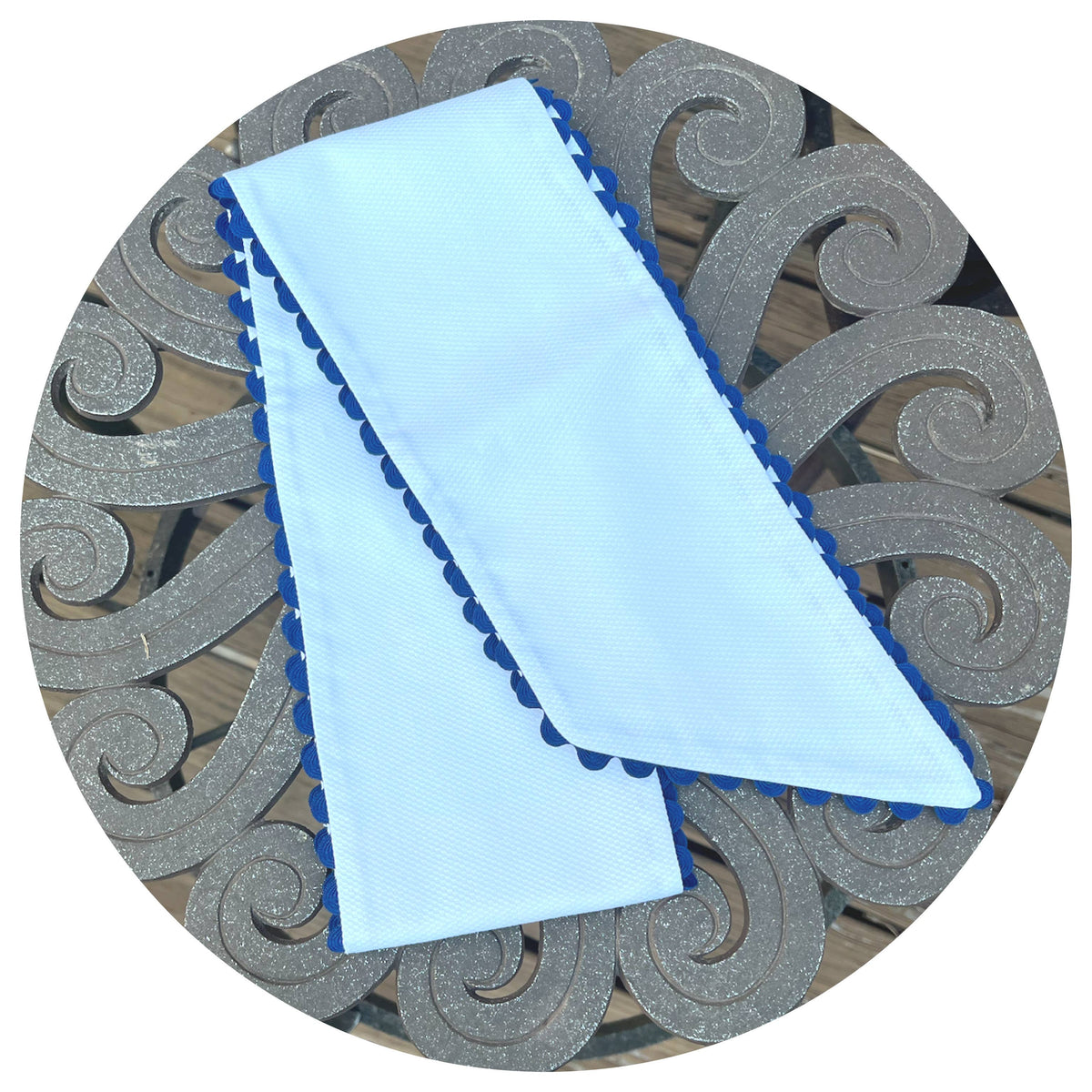 Folded white cotton pique fabric with navy blue scalloped trim, styled on an ornate metal outdoor table