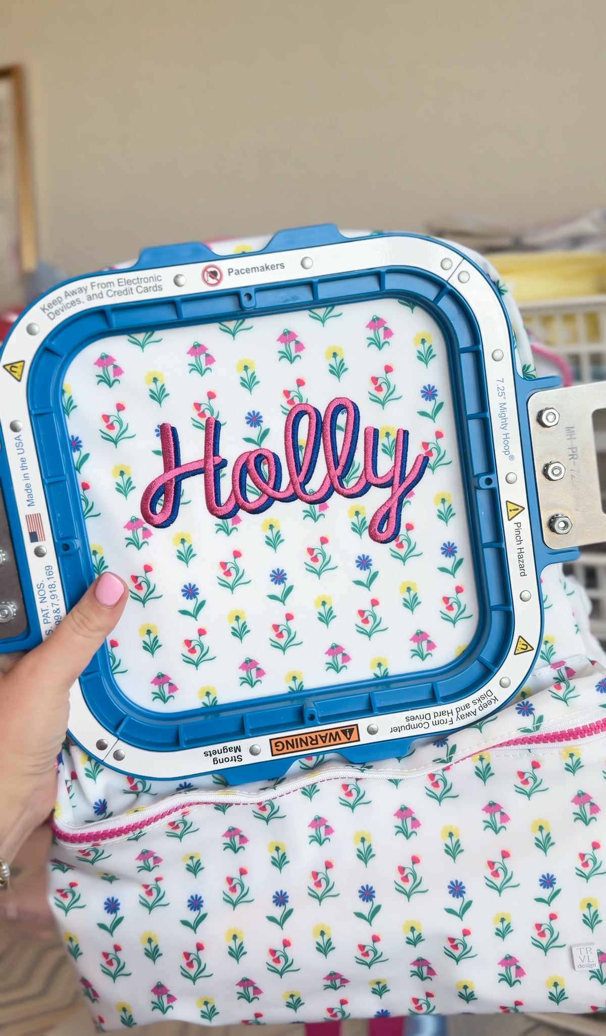 Close-up of an embroidery machine stitching the name 'Holly' onto a white floral print bag