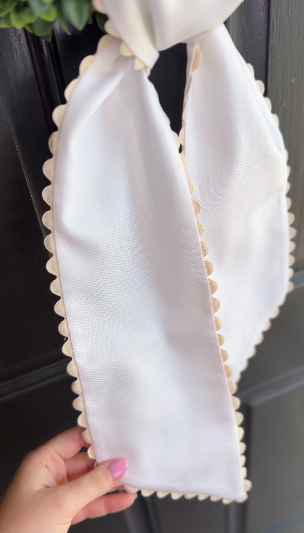 White wreath sash held by a hand against a dark background